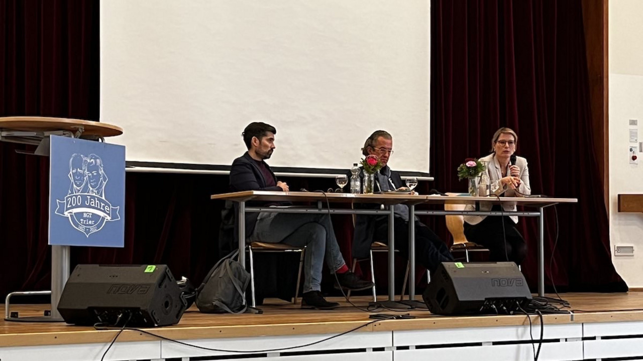 Bildungsministerin Dr. Stefanie Hubig, Landtagsabgeordneter Sven Teuber und Joachim Streit diskutieren in der Aula des Humboldtgymnasiums in Trier mit Schülerinnen und Schülern.