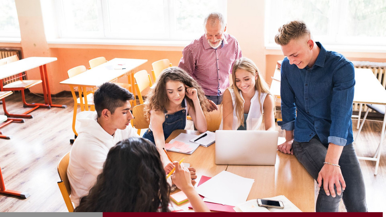 Mehrere Schülerinnen und Schüler arbeiten gemeinsam. Im Hintergrund ist eine Lehrkraft zu sehen. 