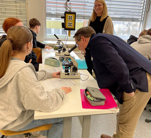 Auf dem Bild ist ADD-Präsident Linnertz mit Schülerinnen und Schülern während des Biologieunterrichts zu sehen. Linnertz schaut durch ein Mikroskop. 