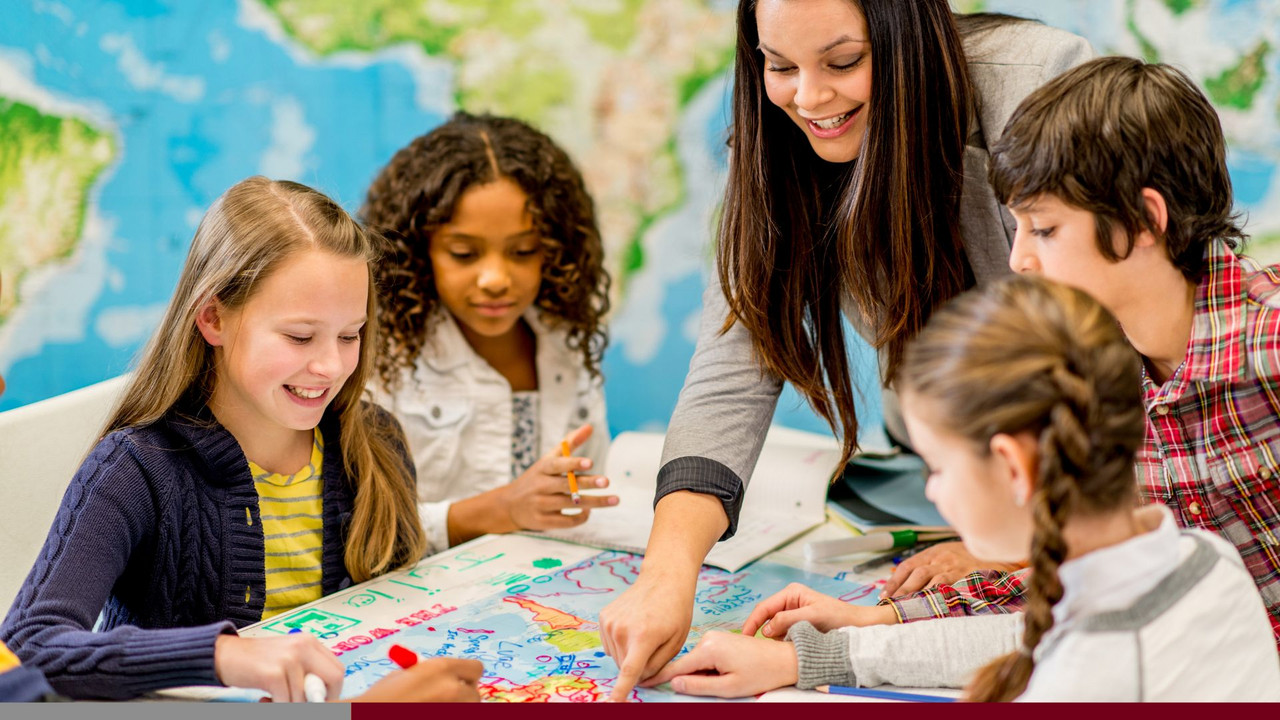 Vier Kinder arbeiten gemeinsam an einem Gruppenprojekt. Eine Lehrkraft betreut die Kinder. 