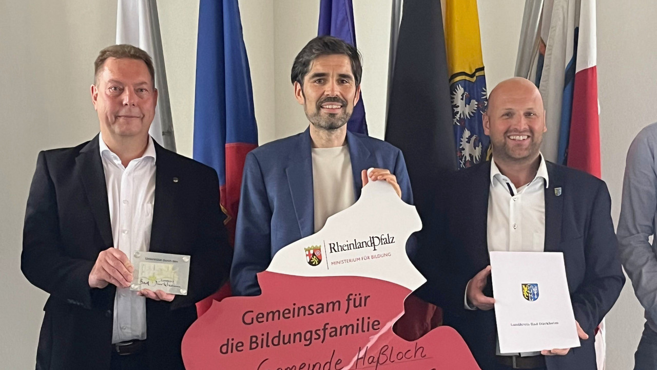 Auf dem Foto von links nach rechts zu sehen sind: Carsten Brock, Ersten Beigeordnete der Gemeinde Haßloch,  Bildungsminister Sven Teuber sowie der Erste Beigeordneter des Kreises Bad Dürkheim, Timo Jordan. Alle drei halten gemeinsam den in den Umrissen des Landes Rheinland-Pfalz gestalteten Förderbescheid in die Kamera. 