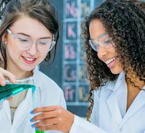 Junge Frauen experimentieren in Laborkitteln.