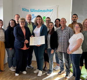 Ein Gruppenbild während der Bescheidübergabe. Zusehen sind Staatssekretärin Brück und die Mitarbeiterinnen und Mitarbeiter der Kita. 